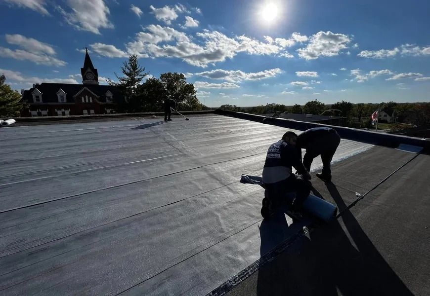 Workers installing roofing on a flat roof under a bright sun and blue sky
