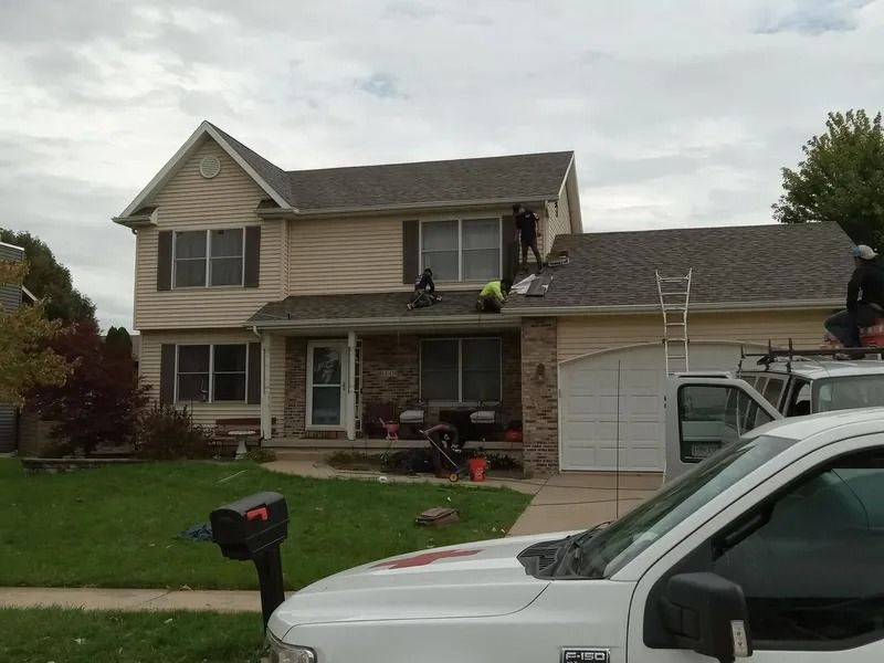 Suburban two-story house with a garage, lawn, and parked vehicles on a cloudy day