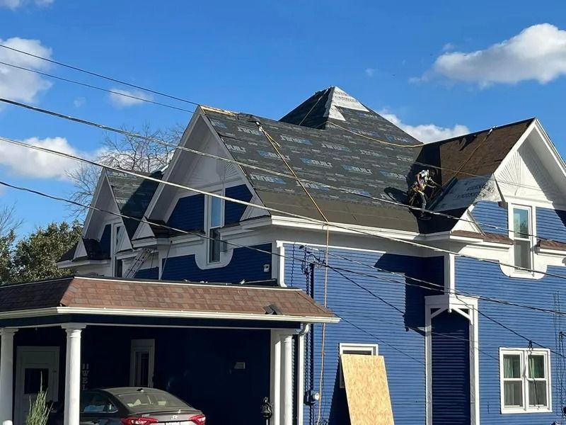 Blue house with severe roof damage and exposed openings, seen from the front under a clear sky