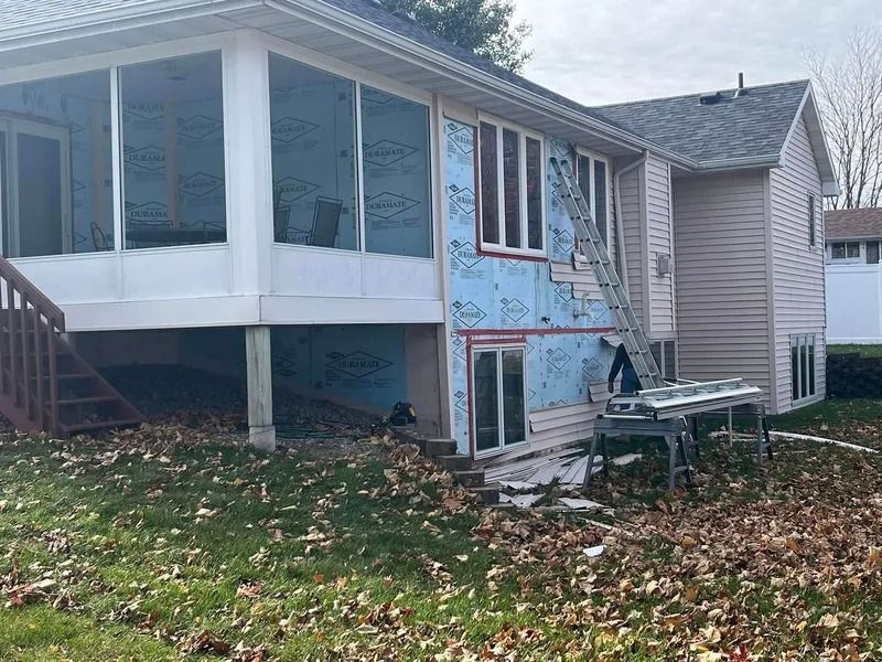House exterior with damaged blue siding and a screened porch, with construction materials on the lawn