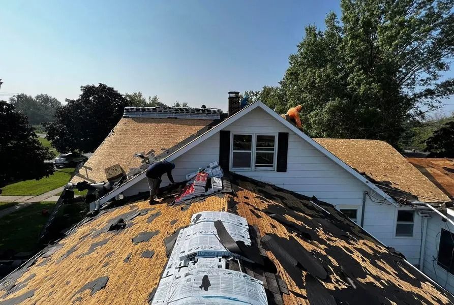 Workers repairing a shingle roof on a house under a blue sky