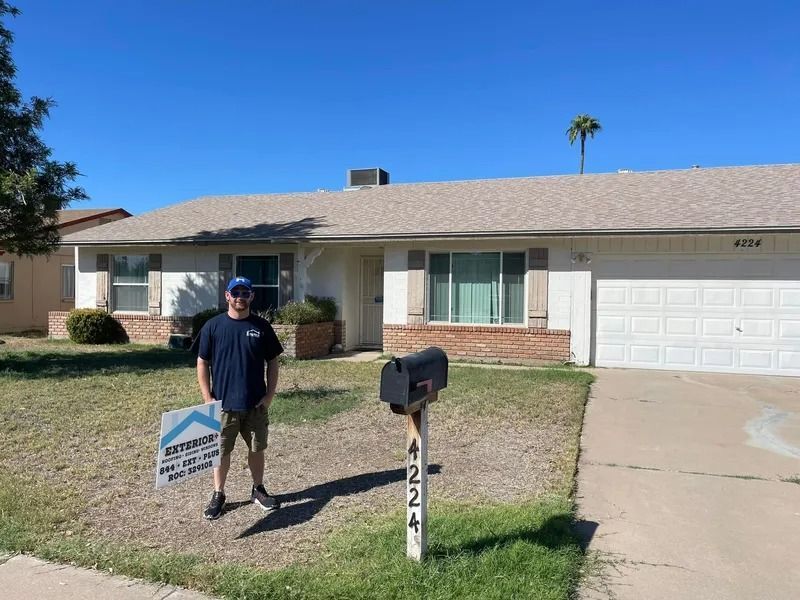 Man standing by a mailbox in front of a single-story house with a garage and blue sky