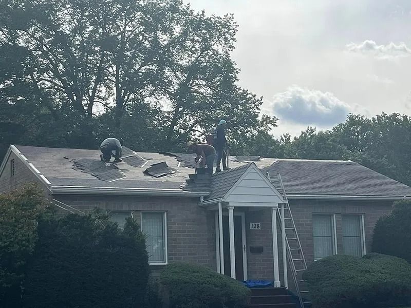 Two workers on a roof repairing shingles on a single-story house