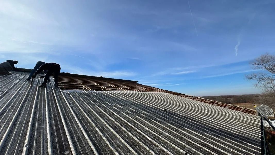 Two workers on a metal roof installing solar panels under a blue sky.