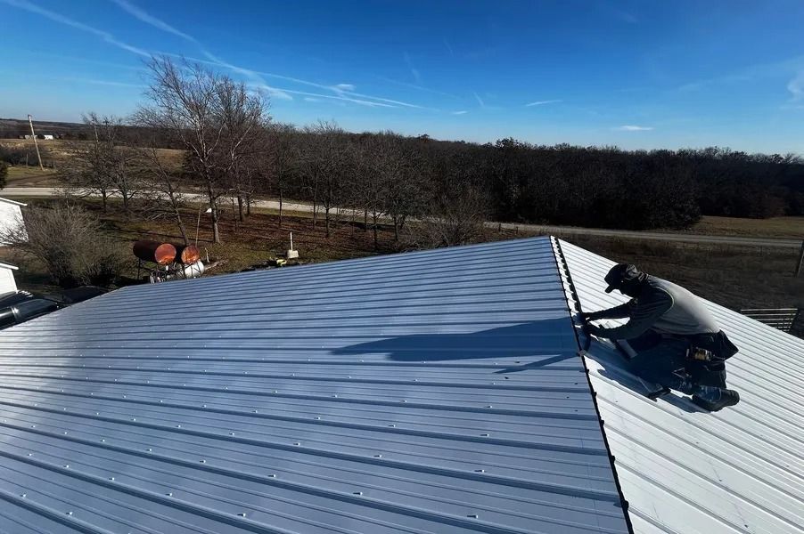 Blue metal roof with a partially installed white section and tools on top, under a clear sky