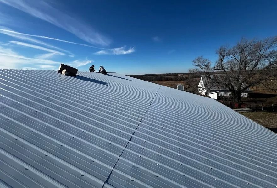 Workers on a corrugated metal roof under a blue sky, with a house and trees in the background