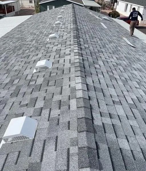 Gray shingle roof with several white vent boxes, worker inspecting near the edge