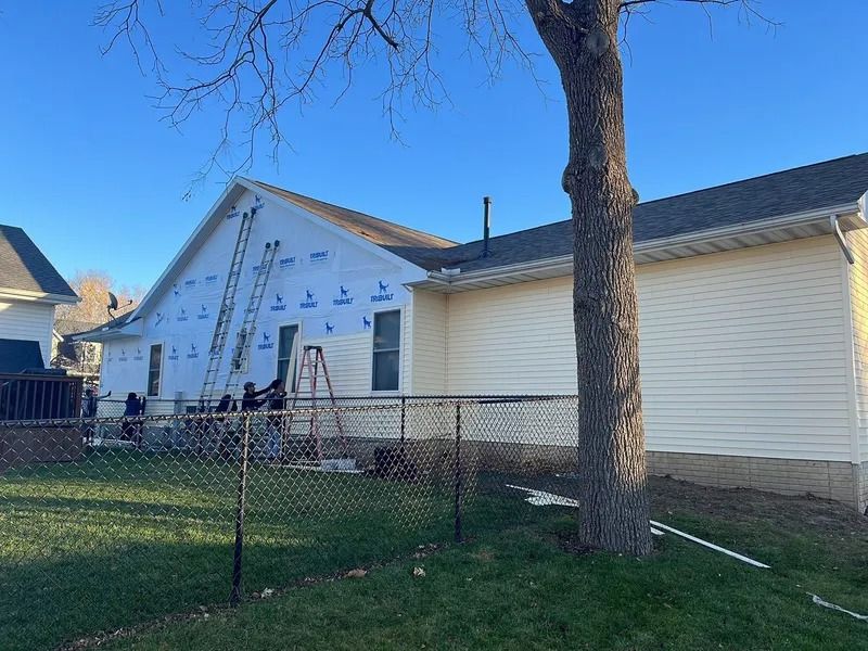 House exterior with white siding, a large tree in front, and a chain-link fence in the yard