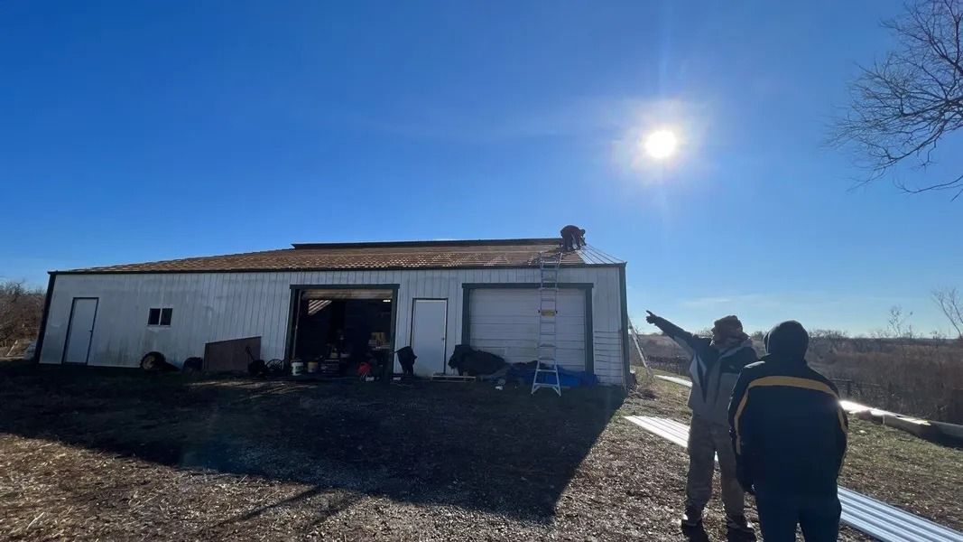 Two people standing by a white barn under a bright sun in a rural field