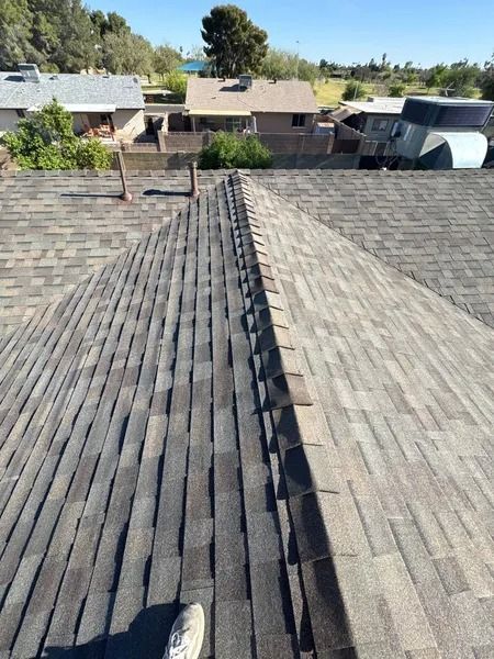 Roof ridge with weathered shingles and neighboring houses in the background under a clear sky