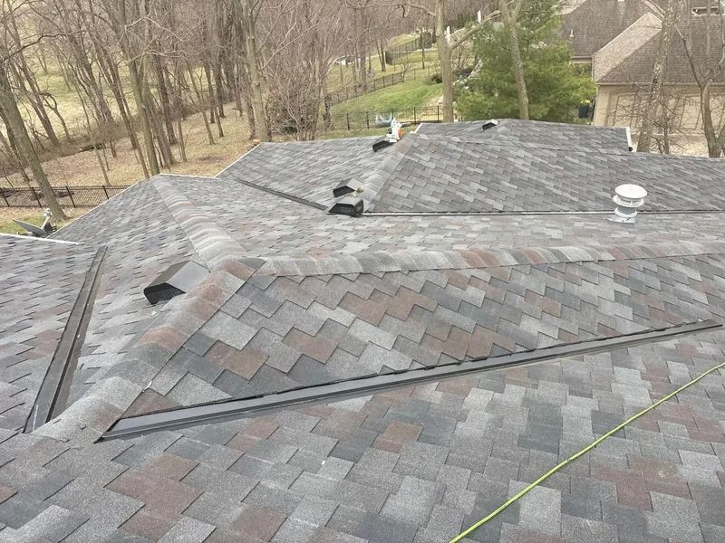 Roof with gray shingles and several vents, seen from above with a measuring tape across it.