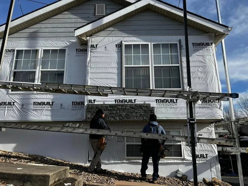 Two workers on scaffolding installing siding on a white house with gray trim