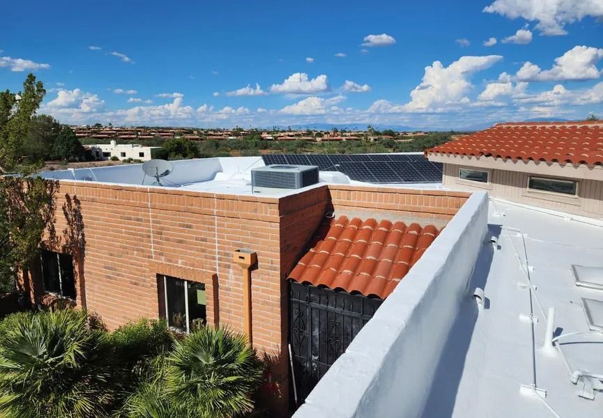 Rooftop view of a brick building with solar panels, terracotta tiles, and blue sky with clouds