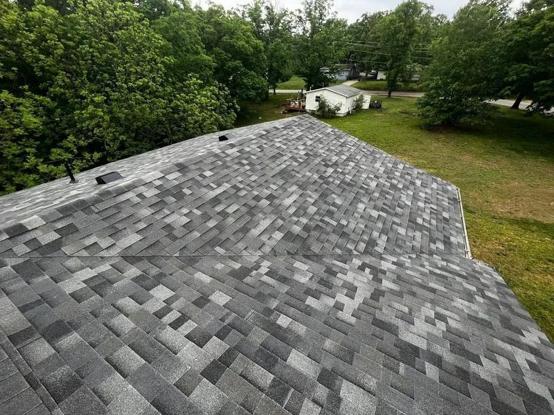 Gray shingled roof viewed from above, with trees and a grassy yard in the background