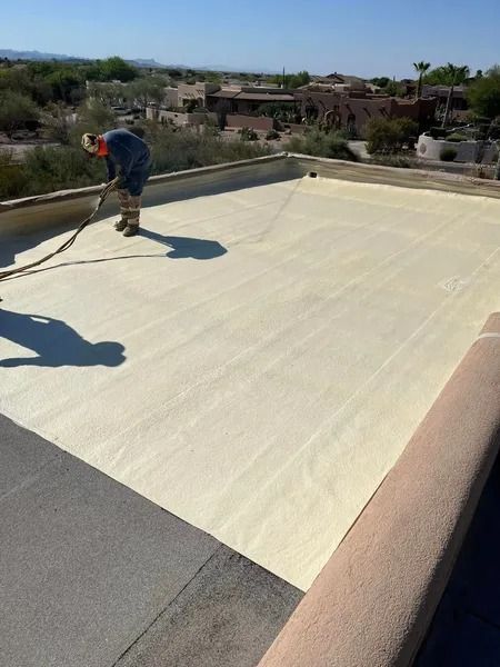 Worker applying white coating to a flat rooftop under a sunny sky