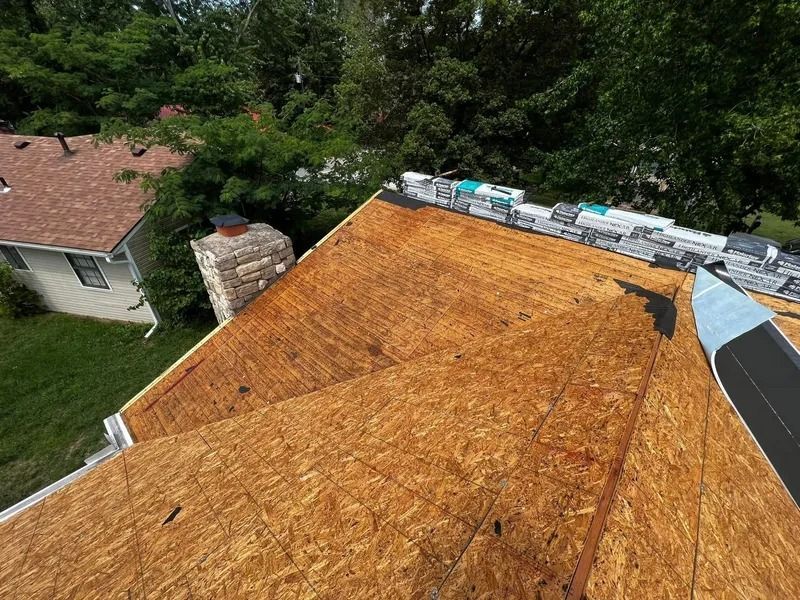 Roof under construction with exposed plywood sheathing and stacks of roofing materials at the ridge