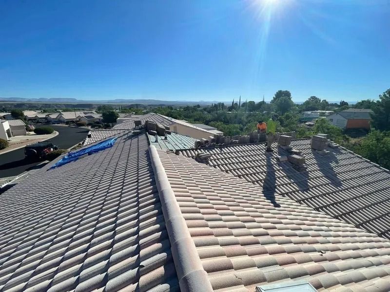 Rooftop with rows of gray tiles under a bright blue sky, with rooftops and trees in the distance