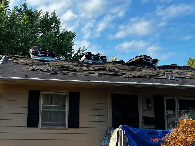 Damaged house roof with missing shingles and debris, under a blue sky
