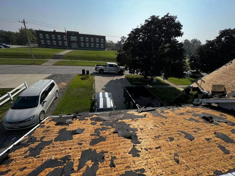 Roof in foreground under repair, with a parked white van, driveway, and apartment building in the distance.