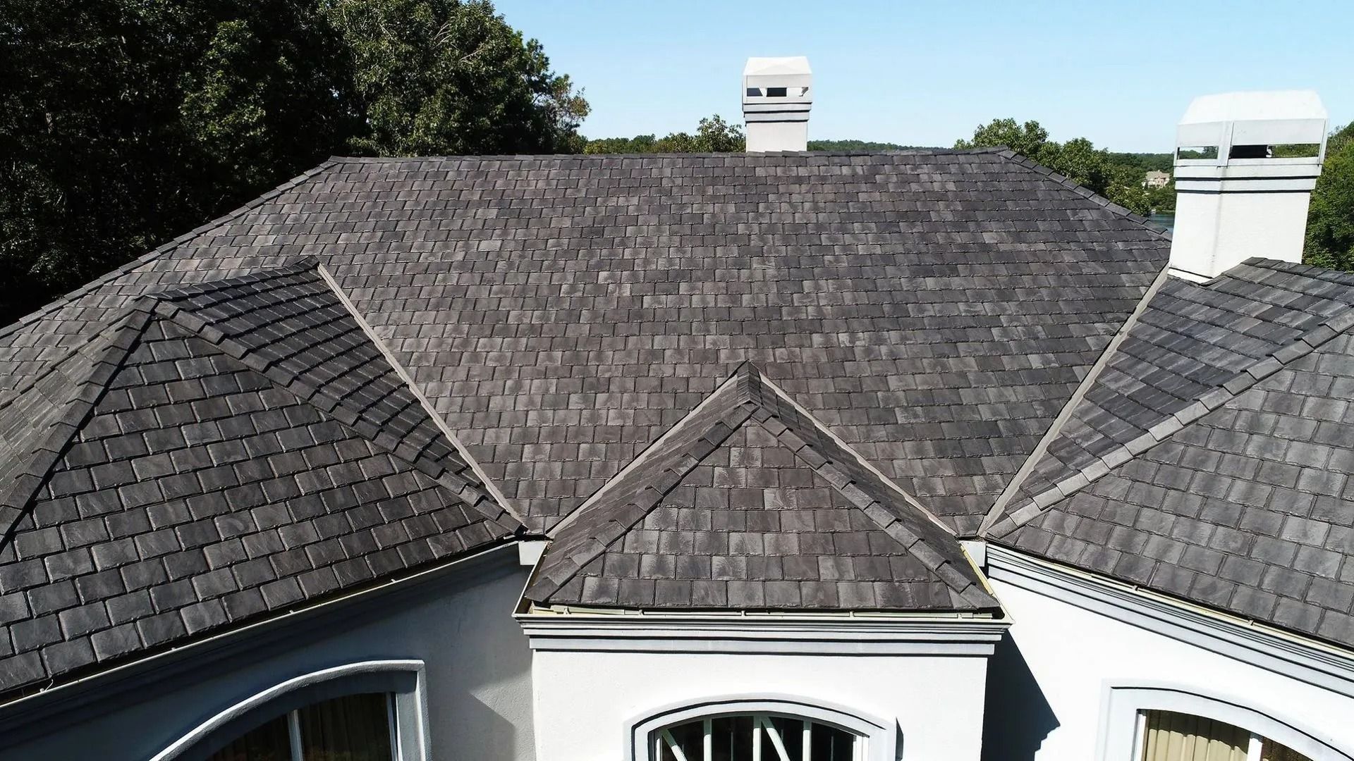 Shingled residential roof with two white chimneys and a small gable over the front entrance