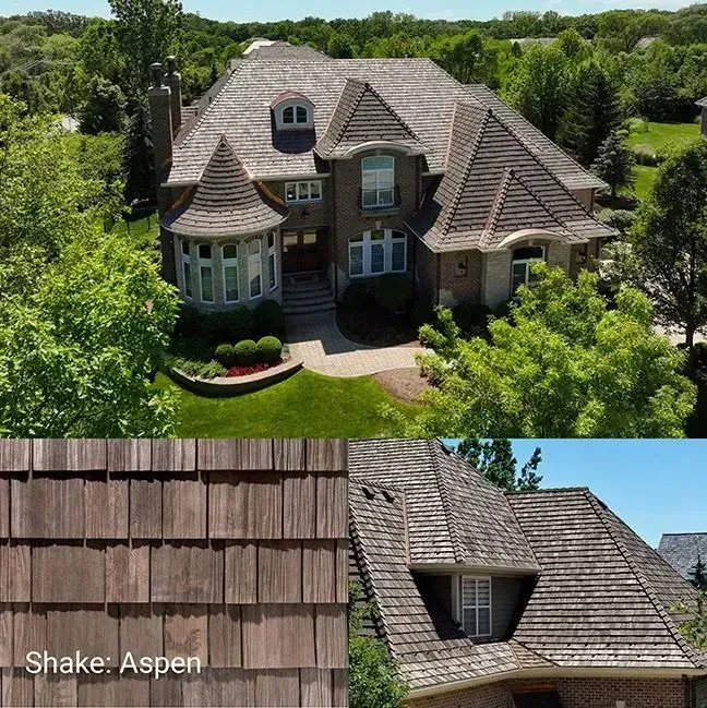 Luxury stone house with gray cedar-shake roof, turreted windows, and lush green landscaping