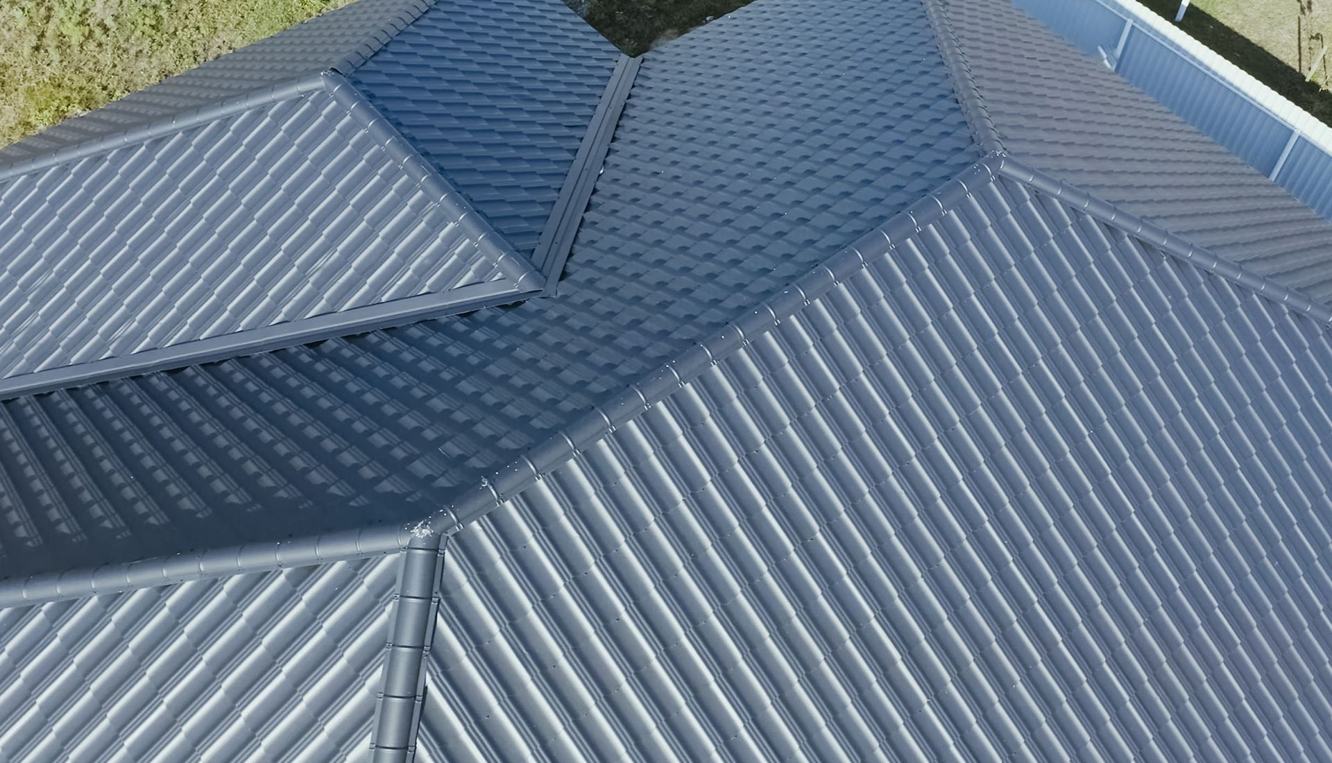 Aerial view of a gray corrugated metal roof with multiple sloped sections and skylight panels