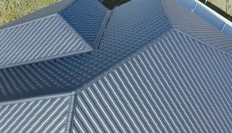 Aerial view of a gray corrugated metal roof with multiple sloped sections and skylight panels