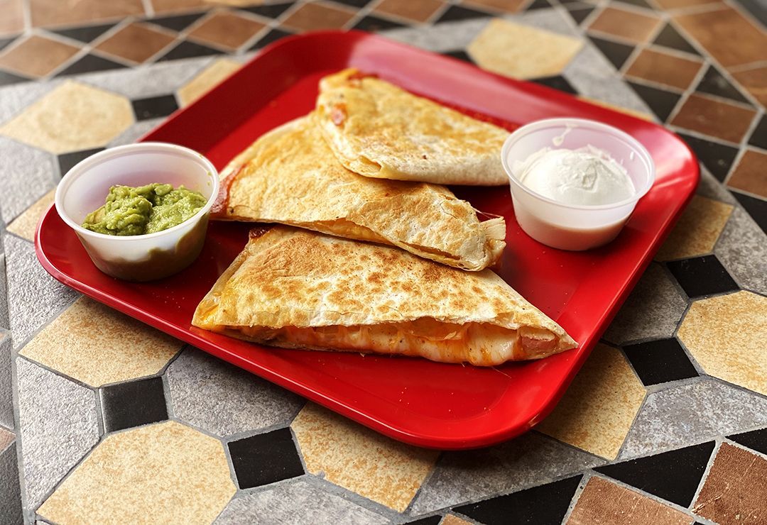 A red plate topped with quesadillas guacamole and sour cream.
