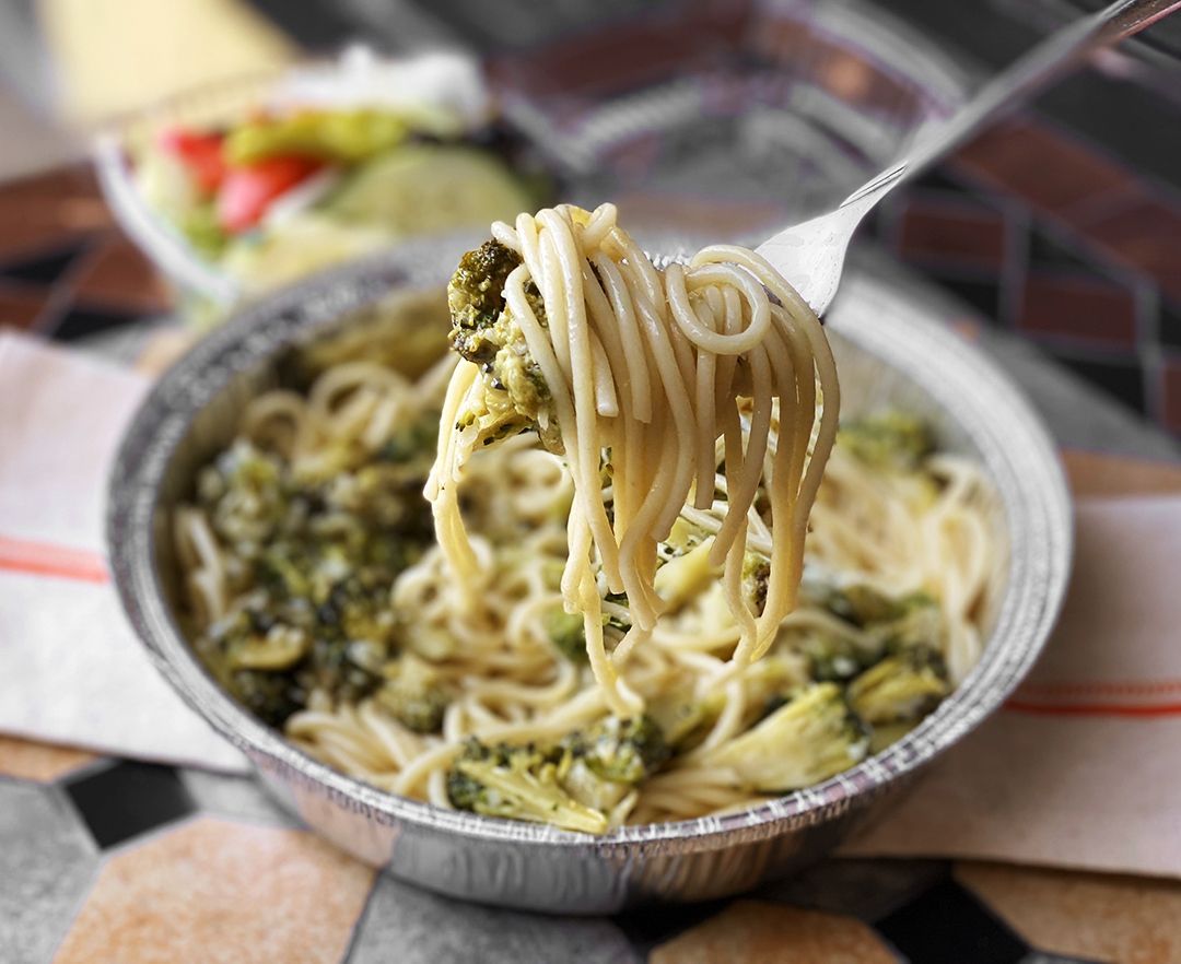 A person is holding a fork over a bowl of spaghetti and broccoli.