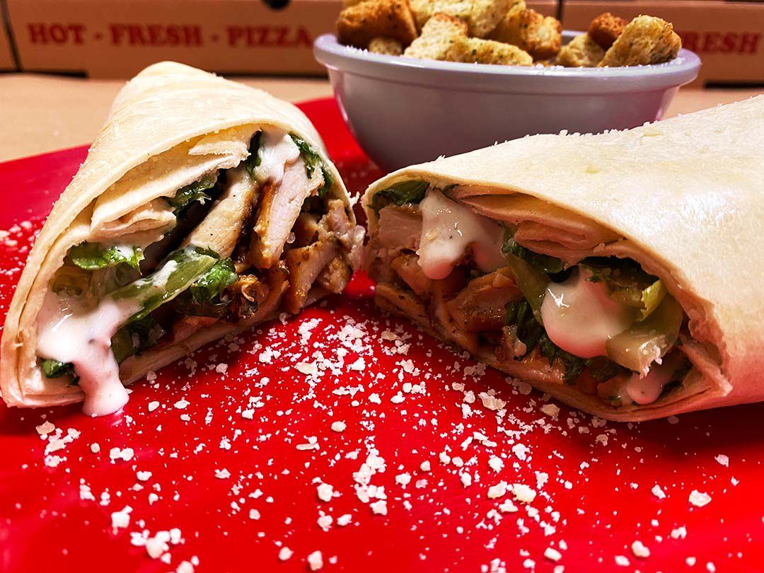 A chicken wrap on a red plate next to a bowl of croutons