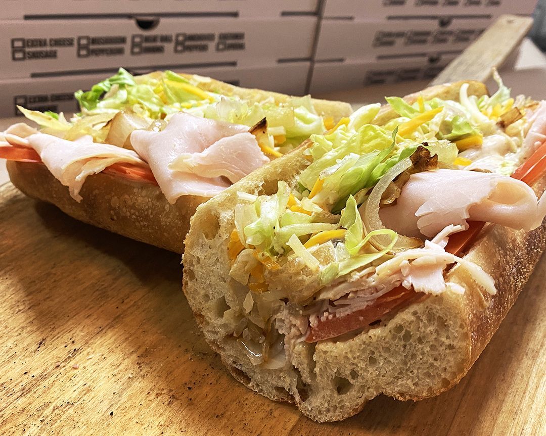 A sub sandwich with turkey, lettuce, tomatoes and cheese on a wooden cutting board.