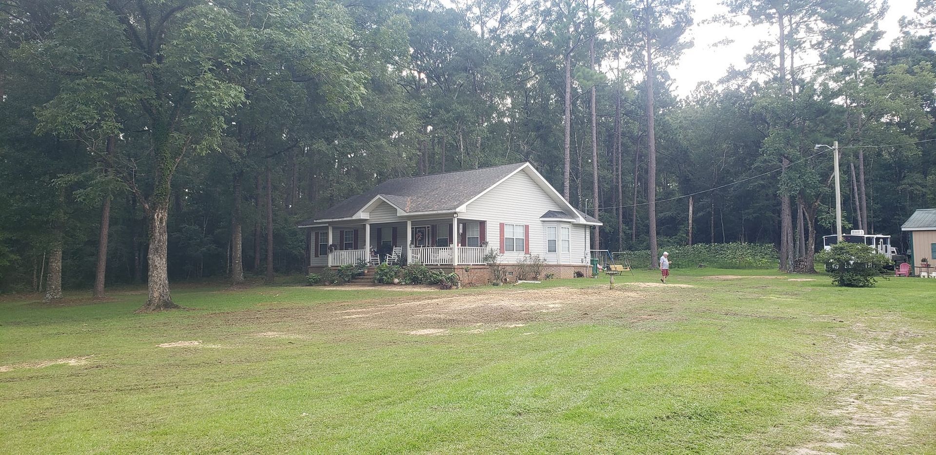 A white house is sitting in the middle of a lush green field surrounded by trees.