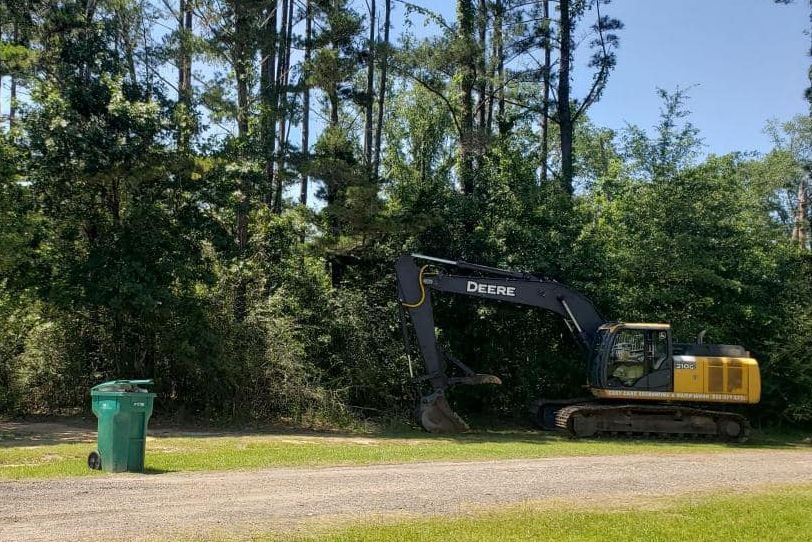 A large excavator is parked in a dirt lot next to a green trash can.
