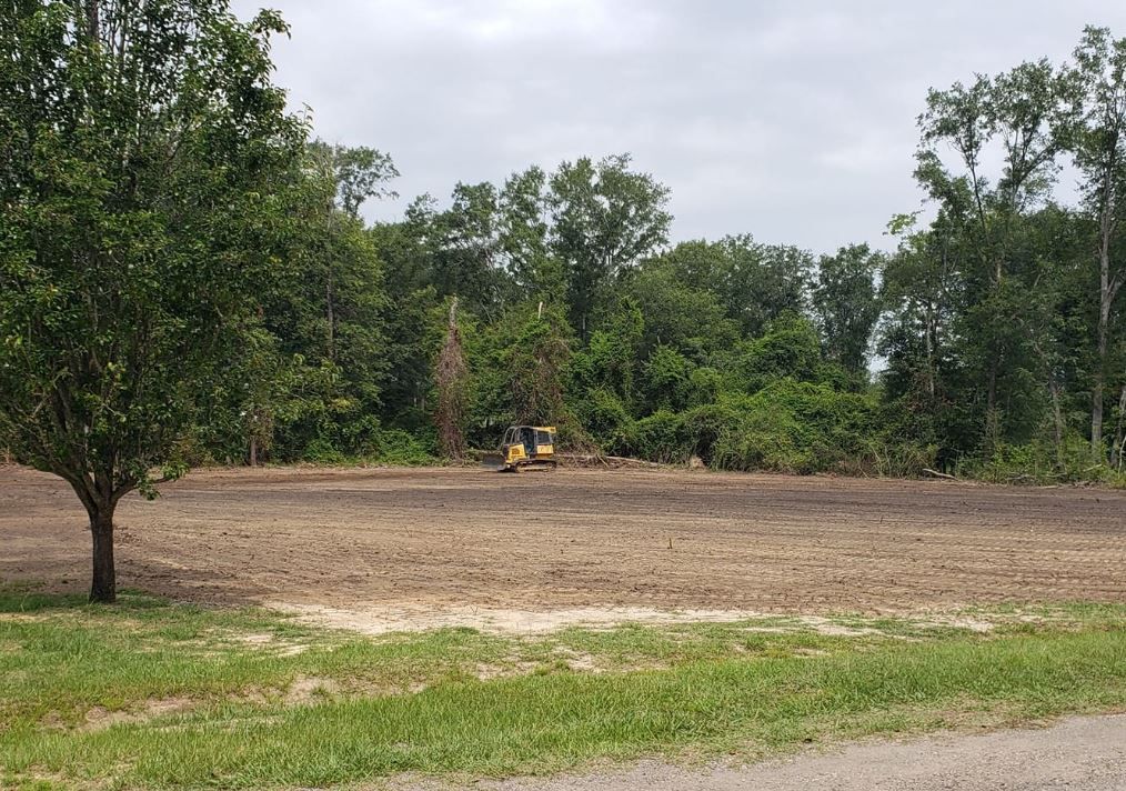 A bulldozer is moving dirt in a field with trees in the background.