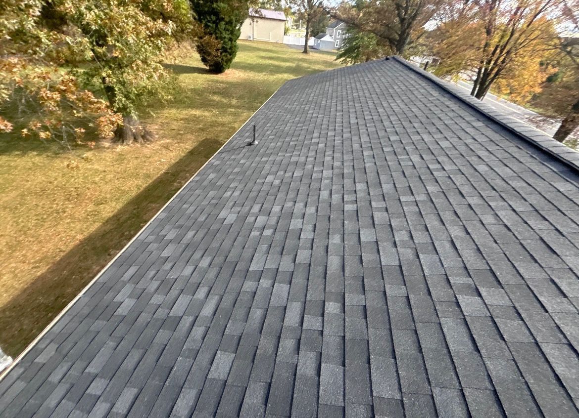 Gray asphalt shingle roof on a house with brown and green yard under trees.
