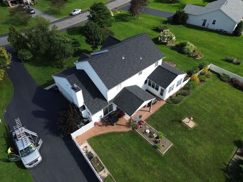 Aerial view of a two-story white house with a dark roof and green lawn. A vehicle parked in the driveway.
