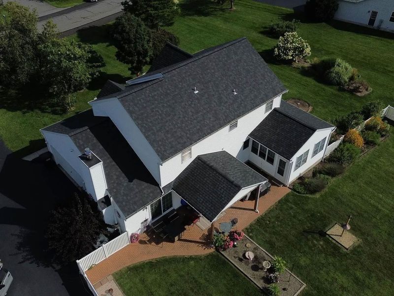 Aerial view of a two-story white house with a dark gray roof, patio, and lush green lawn.