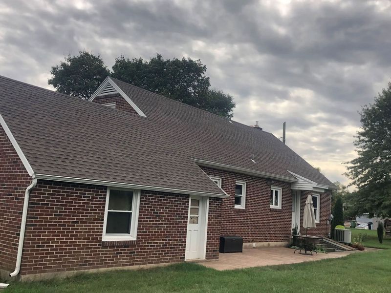 Brick house with a brown shingled roof, white trim, and a cloudy sky.