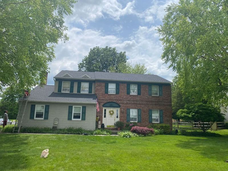 Two-story brick house with new roof. Green shutters, white door, and lush green lawn.