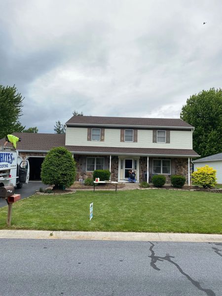 Two-story house with beige siding, brown roof, stone facade, and a well-manicured lawn on a cloudy day.