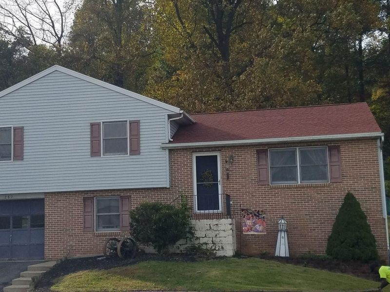 Two-story house with brick and blue siding, red roof, brown shutters, and small garden.