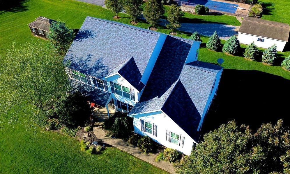 Aerial view of a two-story white house with a gray roof, surrounded by green grass and trees.