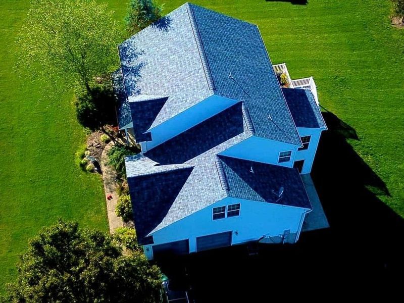 Aerial view of a two-story house with a blue roof and green yard.