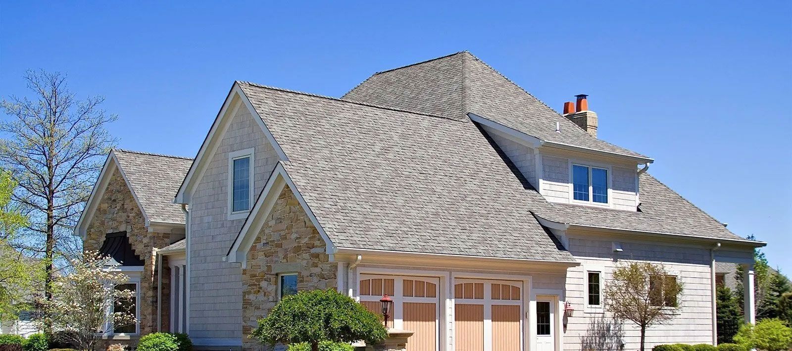 A light gray house with a gray roof and a clear blue sky behind it.