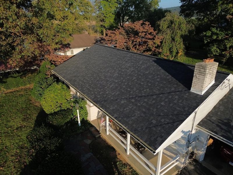 Overhead view of a house with a dark roof, chimney, and porch, surrounded by trees and lawn.