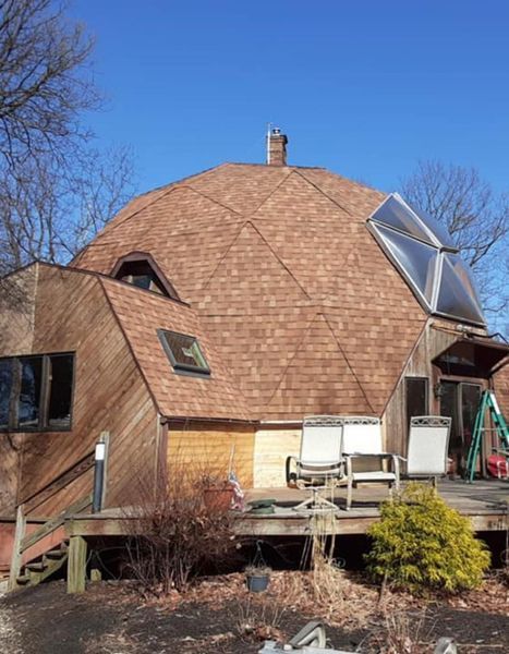 Geodesic dome house with brown roof and wooden siding, set against a blue sky.