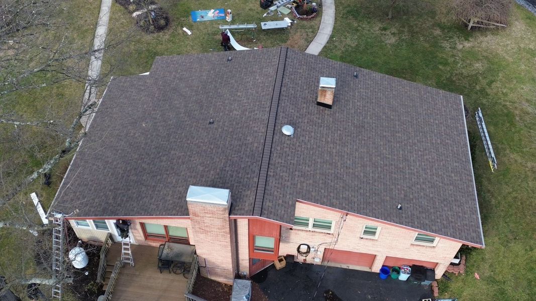 Overhead view of a brown-roofed house with a chimney, garage, and surrounding green yard.