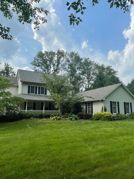 Two-story light green and white house with black shutters, set on a green lawn with trees and a cloudy sky.