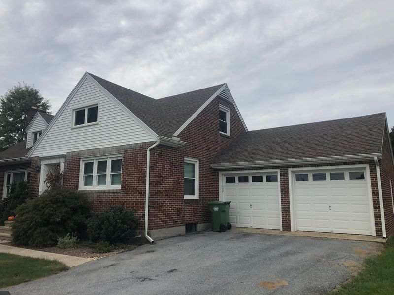 Red brick house with white trim, brown roof, and two-car garage. Cloudy sky overhead.
