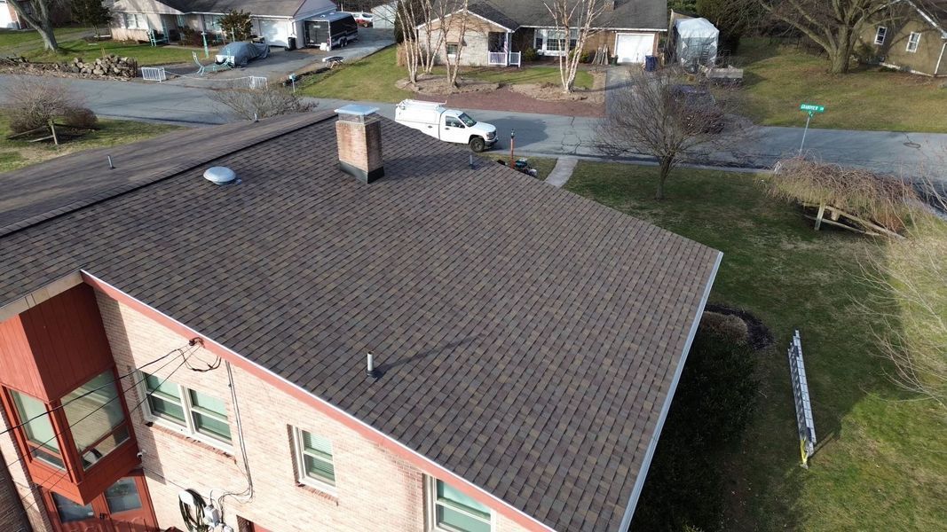 Overhead view of a two-story house with a dark brown shingled roof, chimney, and surrounding neighborhood.
